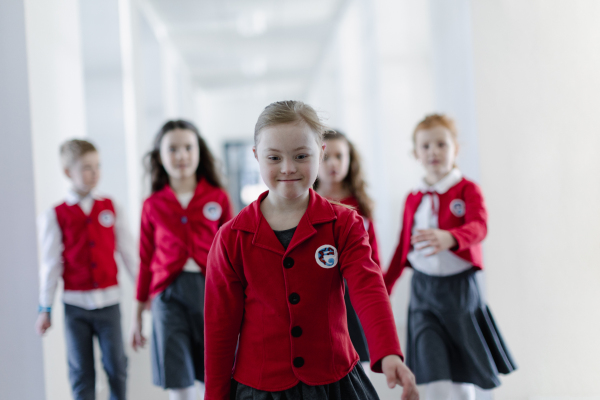 A happy schoolgrirl with Down syndrome in uniform walking in scool corridor with classmates behind her.