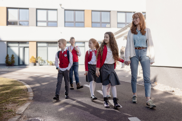 Happy schoolkids in uniforms with teacher walking at schoolyard.