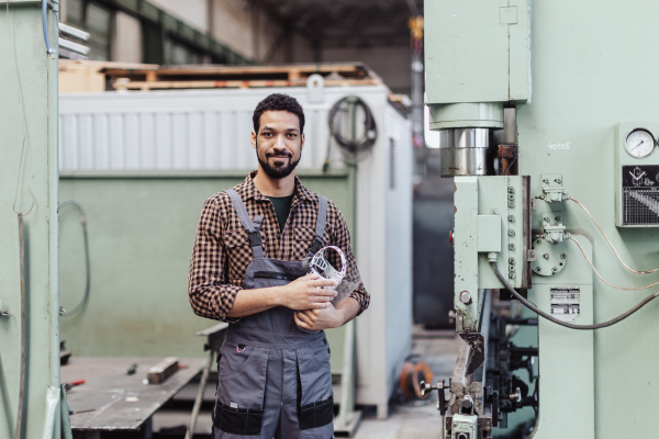 A portrait of engineer male welder standing near metal machine at industrial factory.