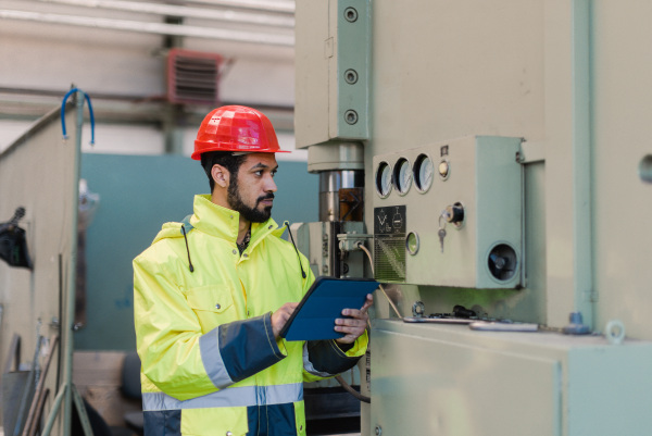 A portrait of engineer male using tablet while checking machines in industrial factory.