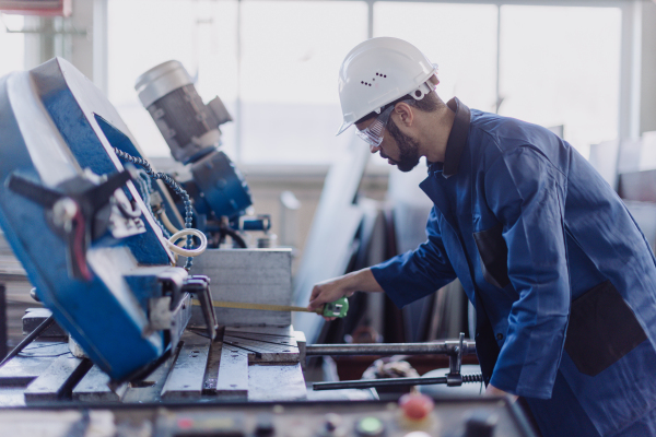 A factory male worker in plant production drilling at metal machine in industrial factory.