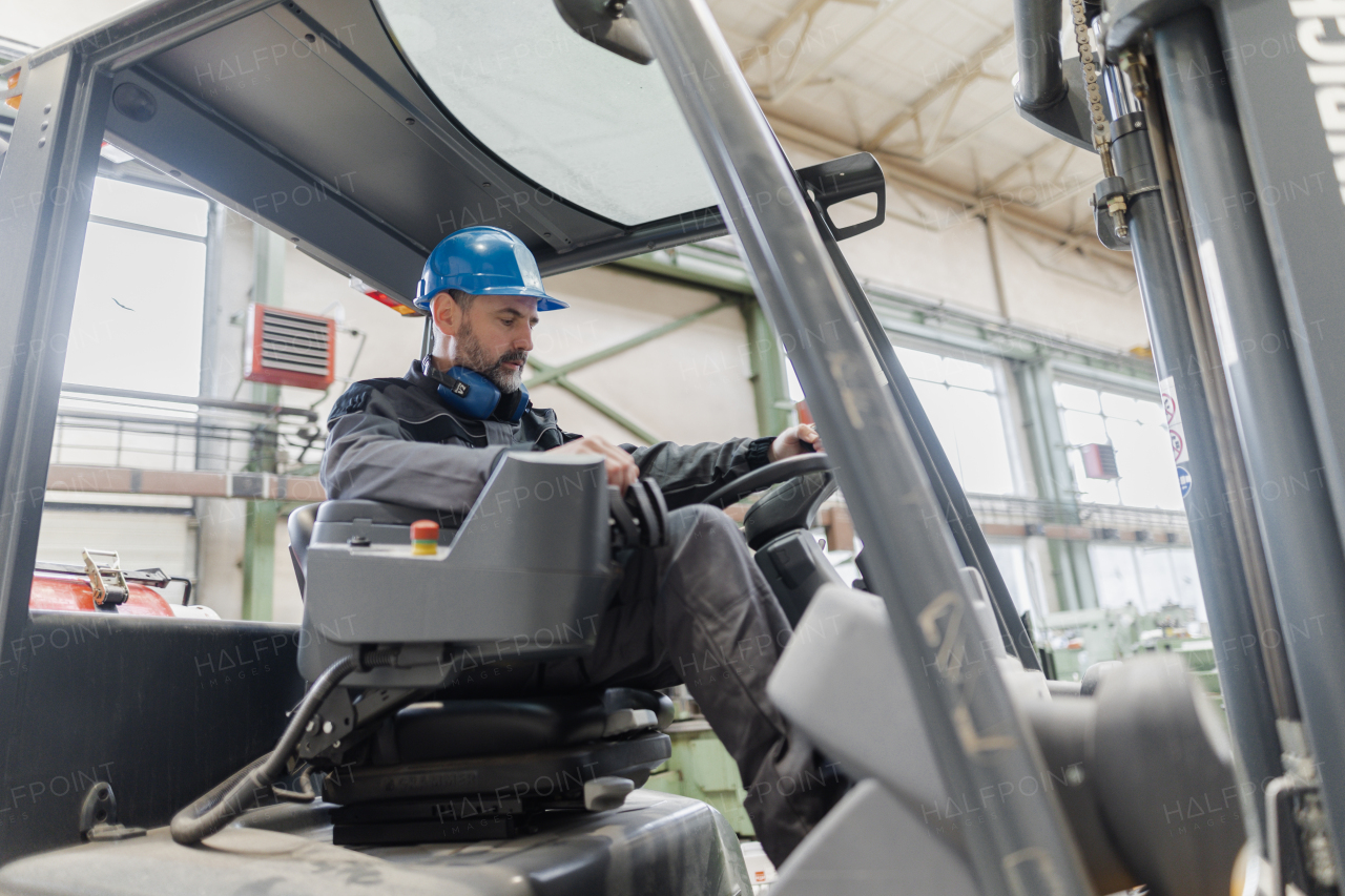 A happy mature man fork lift truck driver lifting pallet in storage warehouse .