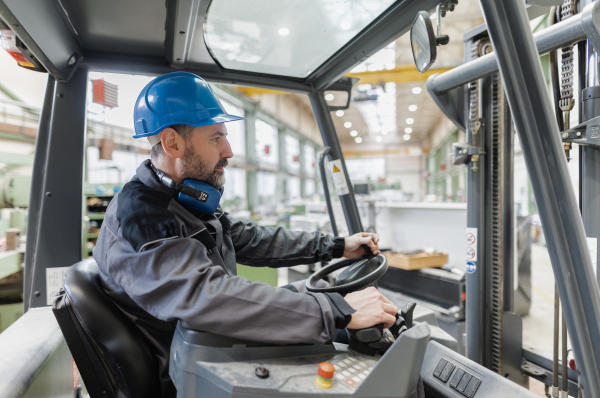 A happy mature man fork lift truck driver lifting pallet in storage warehouse .