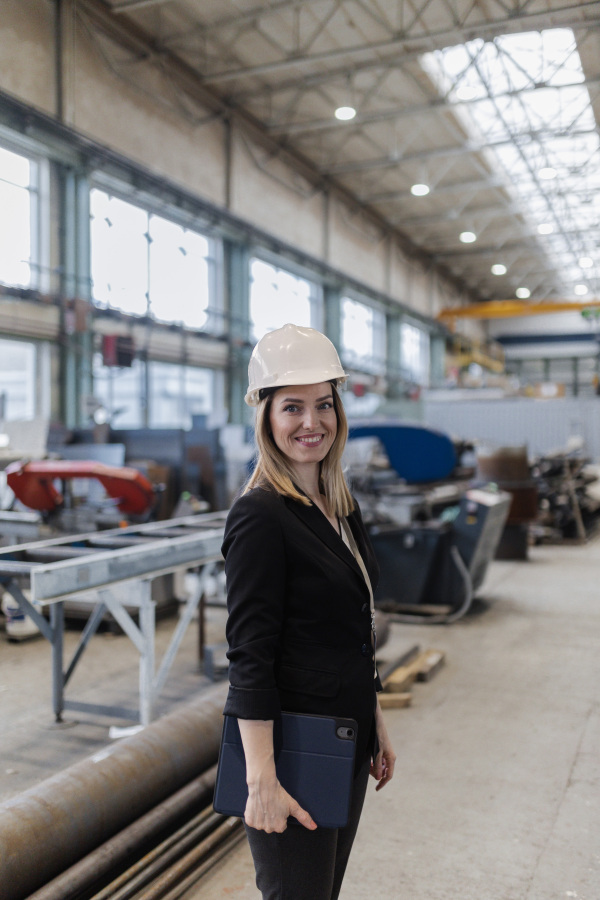 A portrait of female chief engineer in modern industrial factory holding tablet.