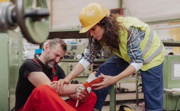 A woman is helping her colleague after accident in factory. First aid support on workplace concept.