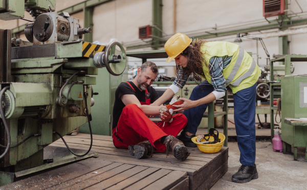 A woman is helping her colleague after accident in factory. First aid support on workplace concept.