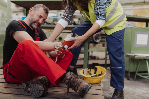 A woman is helping her colleague after accident in factory. First aid support on workplace concept.