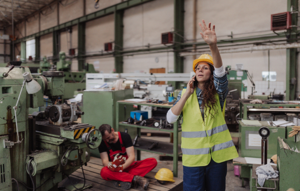 A woman is calling ambulance for her colleague after accident in factory. First aid support on workplace concept.