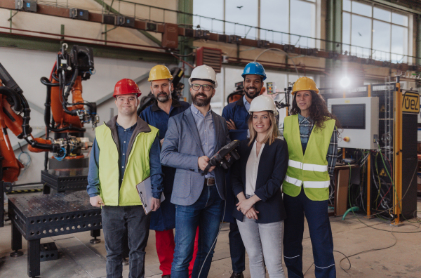 A young man worker with Down syndrome with manager and other collegues working in industrial factory, social integration concept.