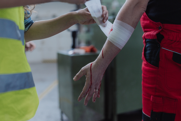 A woman is helping her colleague after accident in factory. First aid support on workplace concept.