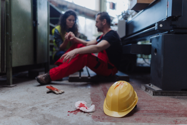 A woman is helping her colleague after accident in factory. First aid support on workplace concept.