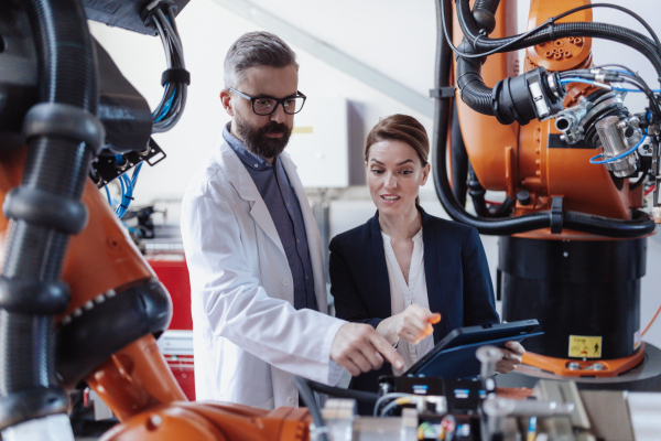 Robotics engineers with a tablet dicussing and desinging modern robotic arm in factory.