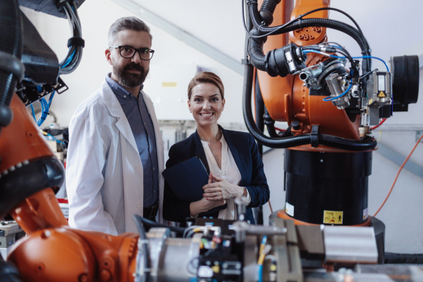 Robotics engineers with a tablet dicussing and desinging modern robotic arm in factory.