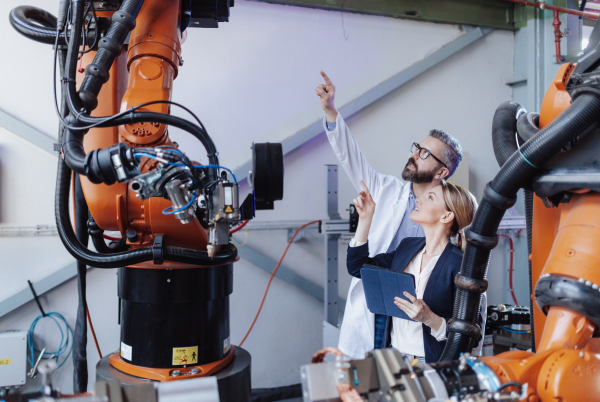 Robotics engineers with a tablet dicussing and desinging modern robotic arm in factory.