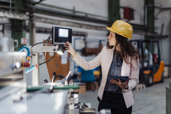 A portrait of female chief engineer in modern industrial factory using tablet and machine.