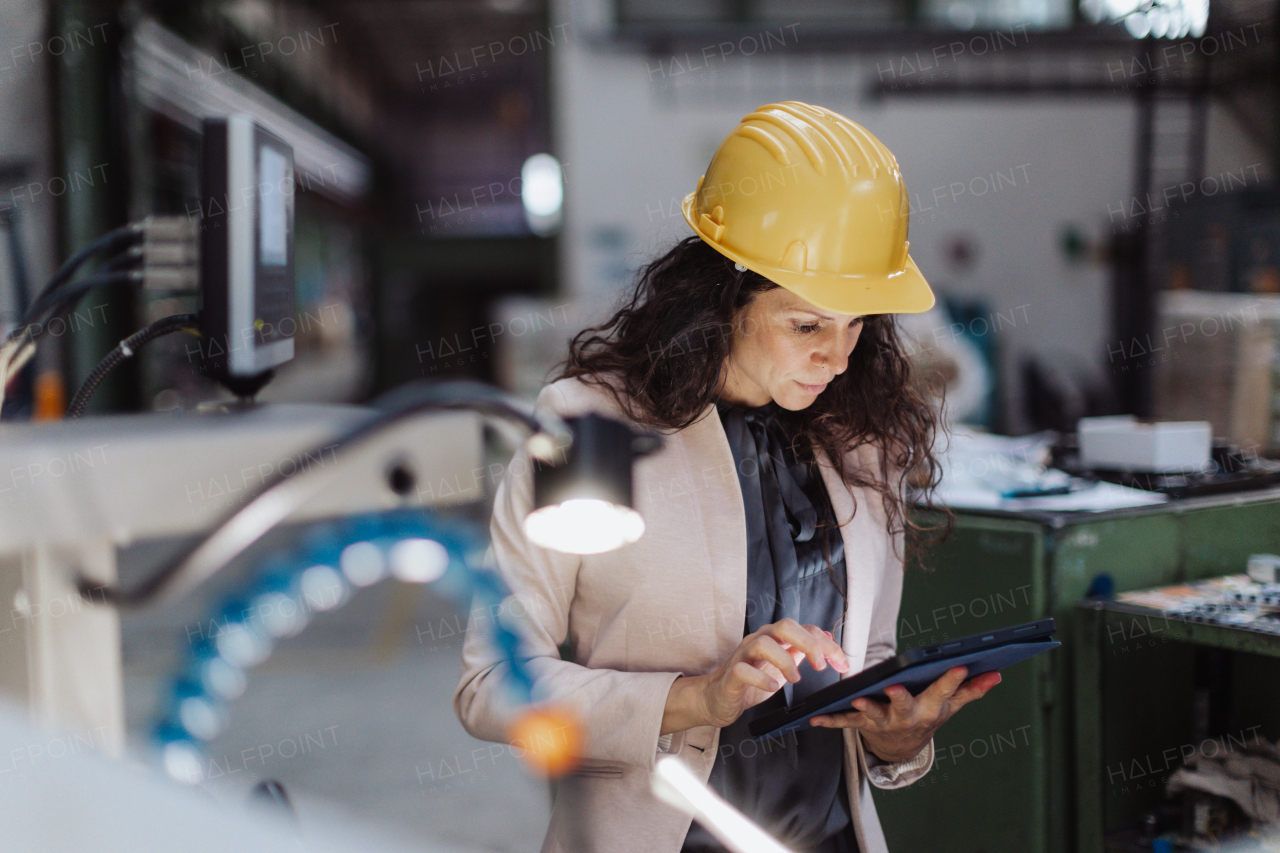 A portrait of female chief engineer in modern industrial factory using tablet and machine.