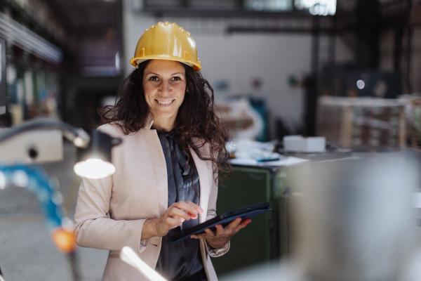 A portrait of female chief engineer in modern industrial factory using tablet and machine.