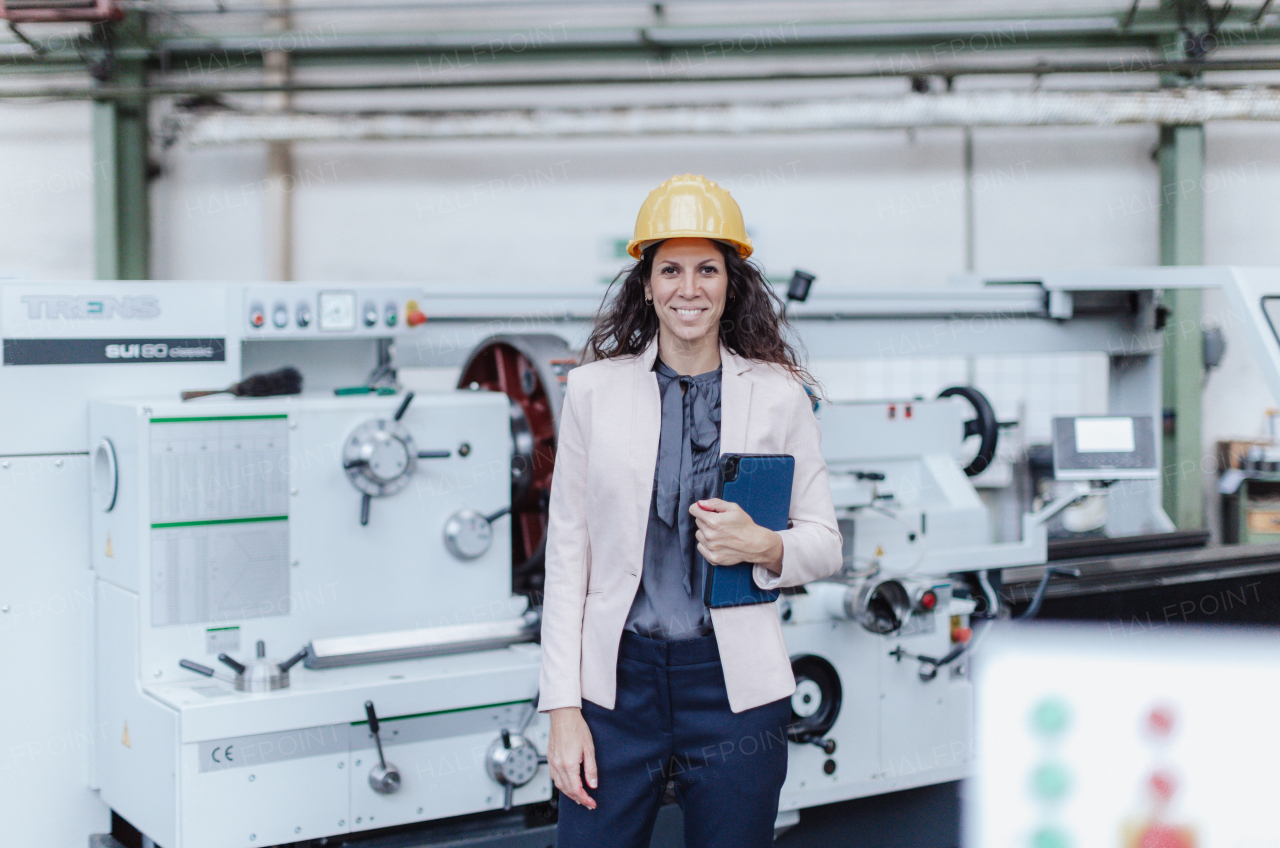 A portrait of female chief engineer in modern industrial factory using tablet and machine.