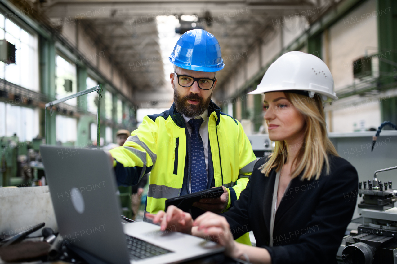 A male and female industrial engineers discussing factory's new machinery project and using laptop.