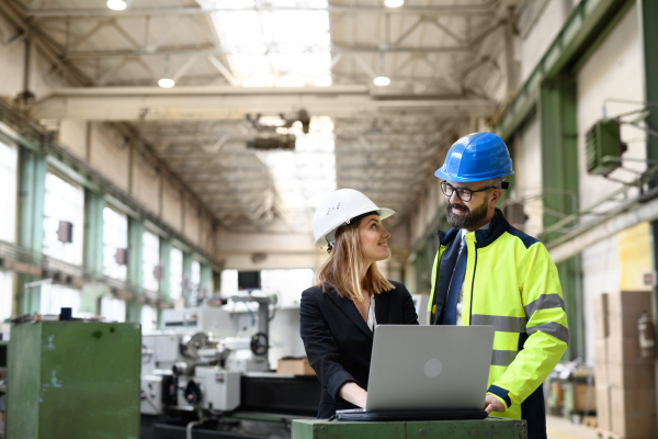 A male and female industrial engineers discussing factory's new machinery project and using laptop.