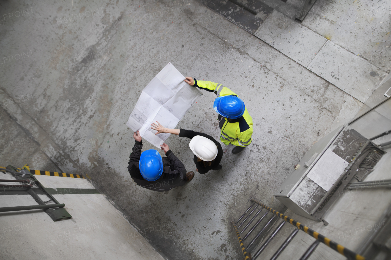 A top view of engineer and industrial worker in uniform shaking hands in large metal factory hall and talking.