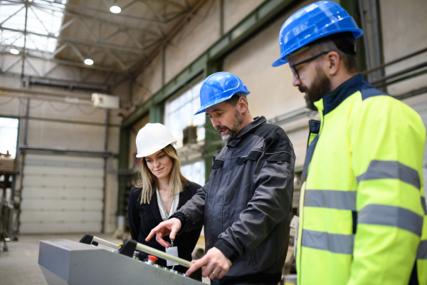 Manager supervisors and a industrial worker in uniform doing control in large metal factory hall and talking.