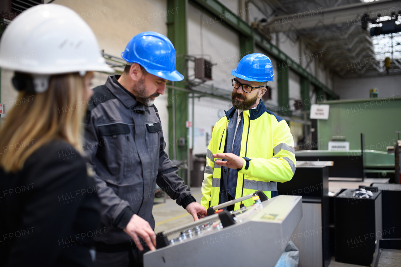 Manager supervisors and a industrial worker in uniform doing control in large metal factory hall and talking.