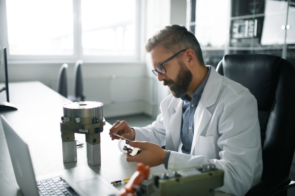 A robotics engineer working on desing of modern robotic arm adn sitting at dest in laboratory.