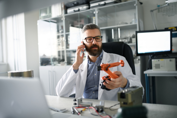 A robotics engineer calling on cellphone and working on desing of modern robotic arm in laboratory office.