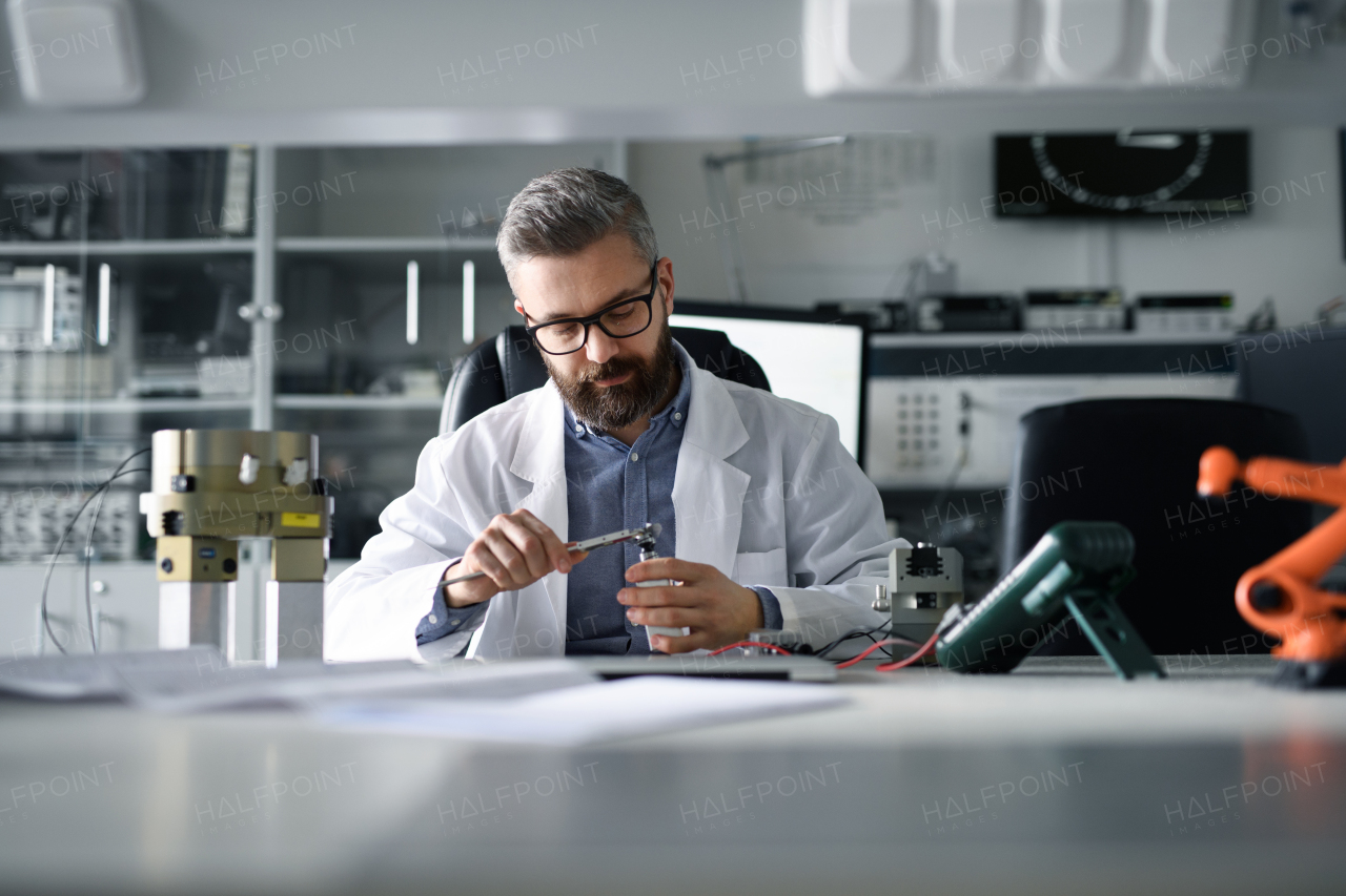 A robotics engineer working on desing of modern robotic arm adn sitting at dest in laboratory.