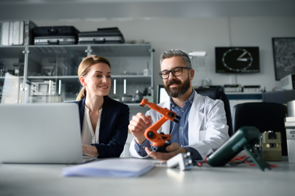 Robotics engineers working on a laptop and desinging modern robotic arm in laboratory.