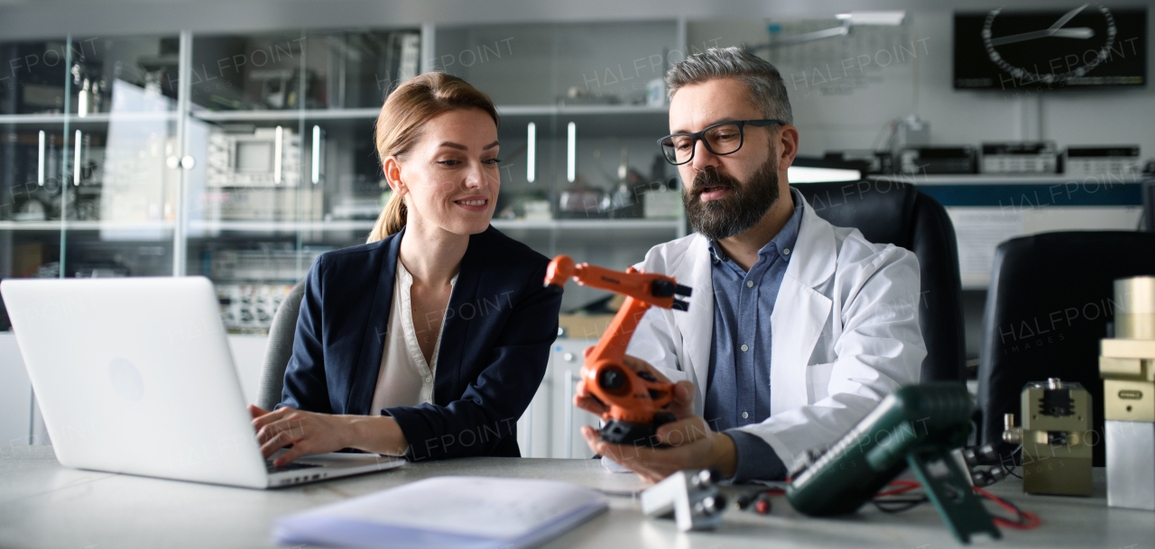 Robotics engineers working on a laptop and desinging modern robotic arm in laboratory.