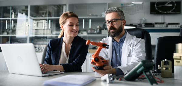 Robotics engineers working on a laptop and desinging modern robotic arm in laboratory.