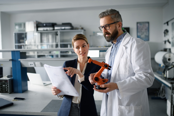 Robotics engineers with blueprints dicussing and desinging a modern robotic arm in laboratory.