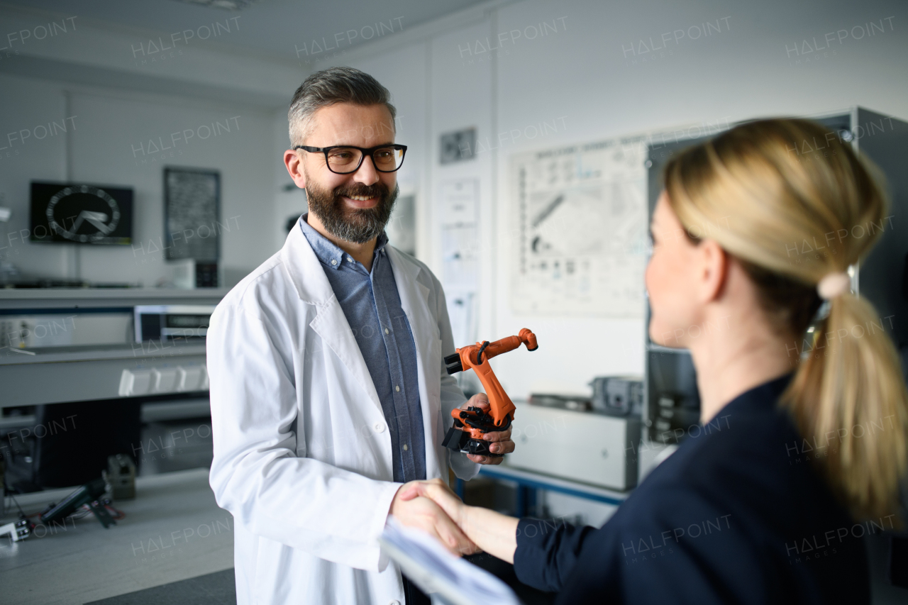 Robotics engineers working and desinging a modern robotic arm in laboratory, shaking hands.