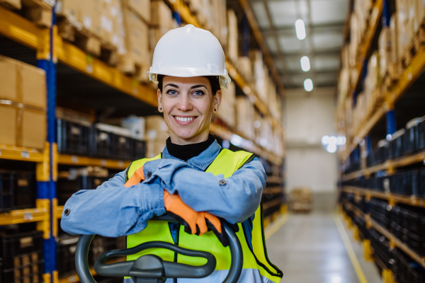 Portrait of a warehouse female worker in reflective vest with a pallet truck.