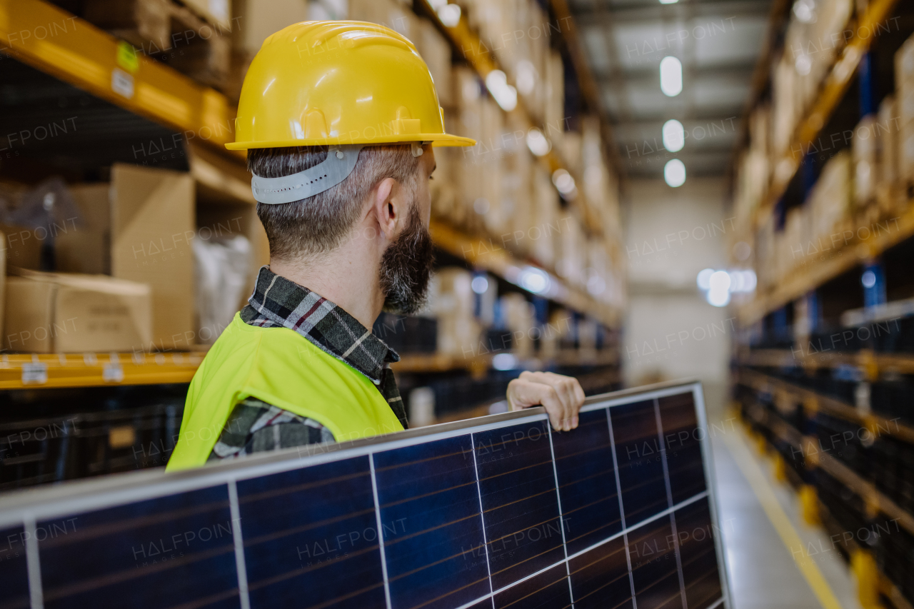 Rear view of warehouse worker carring a solar panel.