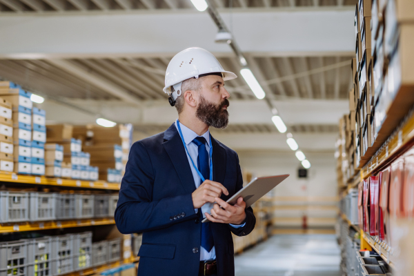 Manager in suit controlling goods in warehouse.