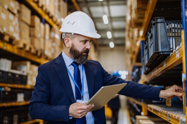 Manager in suit controlling goods in warehouse.