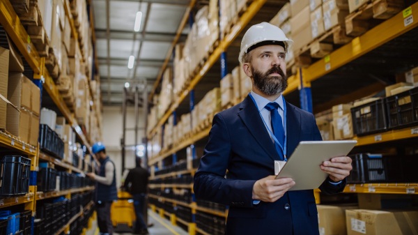 Manager in suit controlling goods in warehouse.