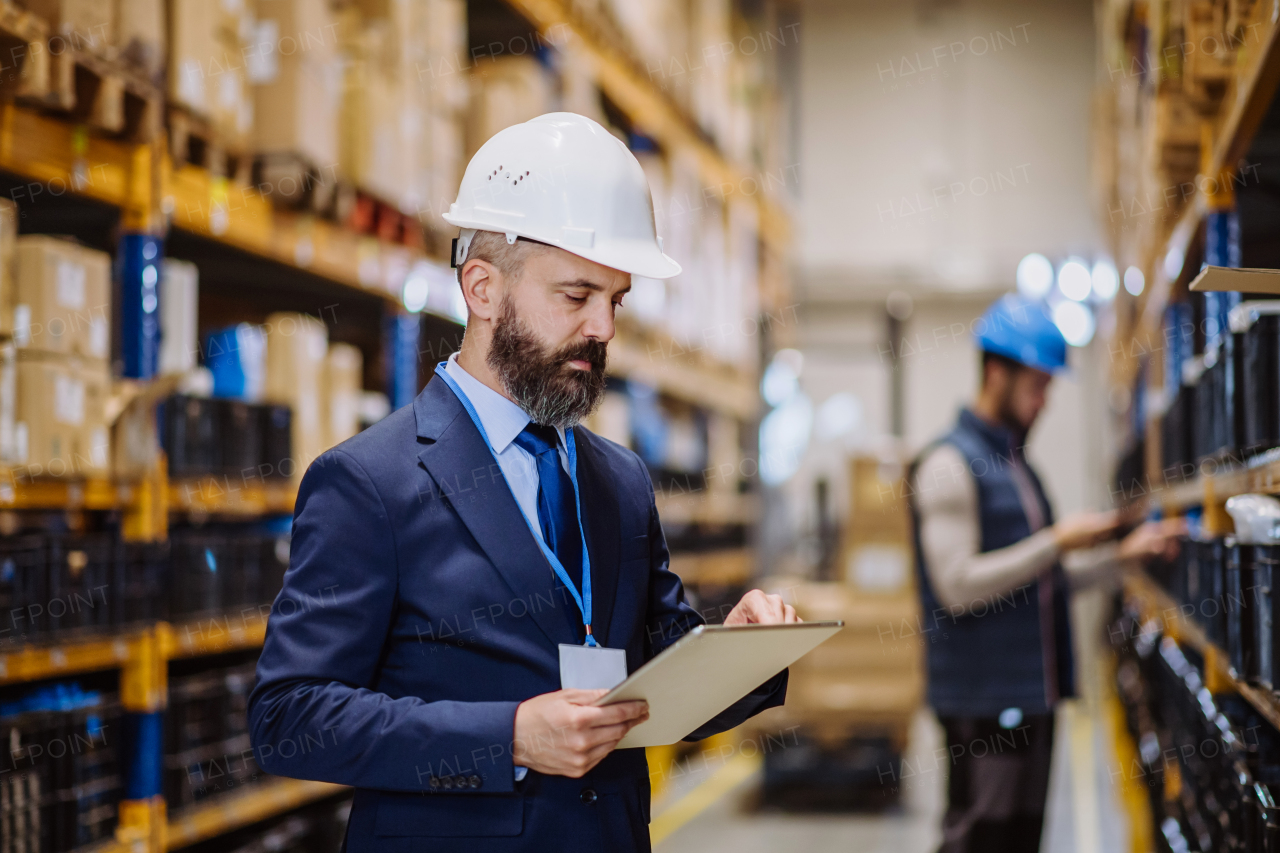 Manager in suit controlling goods in warehouse.