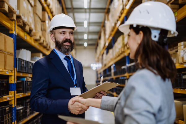 Managers in suits shaking hands in a warehouse.