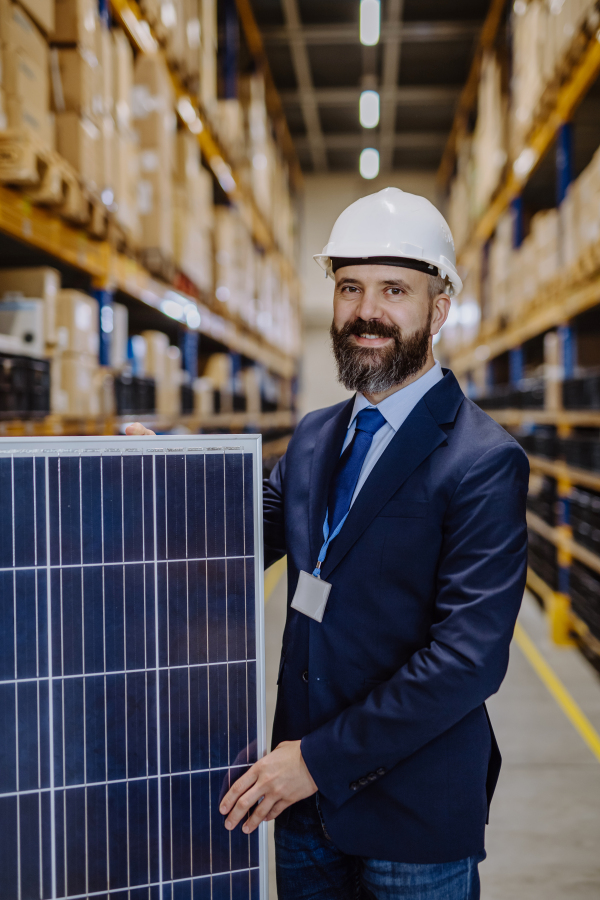 Portrait of manager holding solar panel in a warehouse.