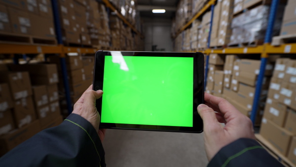 A firstperson view of warehouse worker checking up stuff in a warehouse on tablet with green screen.