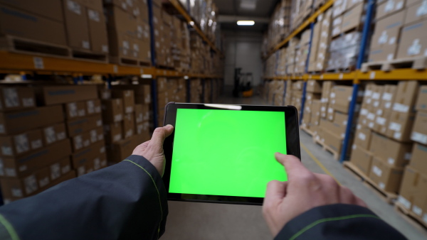 A firstperson view of warehouse worker checking up stuff in a warehouse on tablet with green screen.