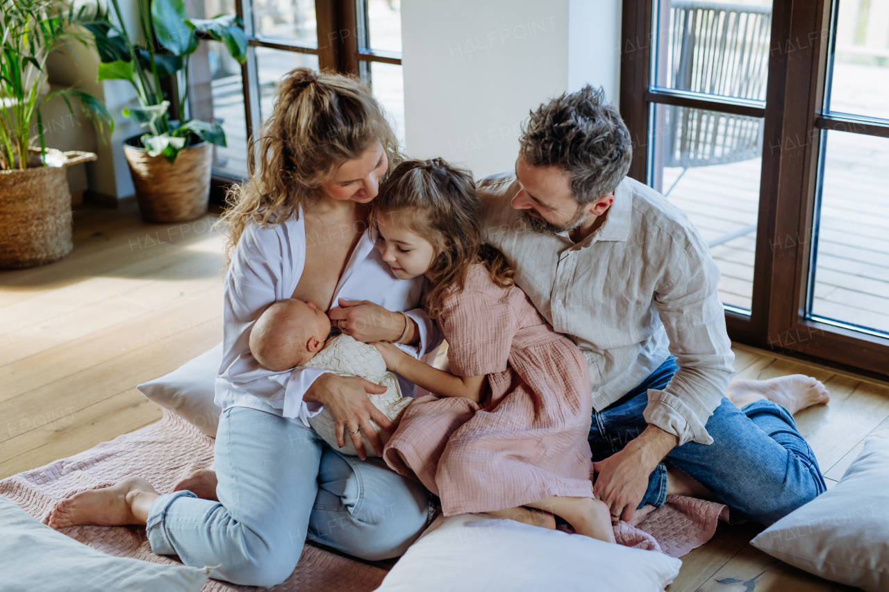 Mother breastfeeding newborn, big sister looking at new baby in mom's arms. Strong family, bonding, parents' unconditional love for their children.