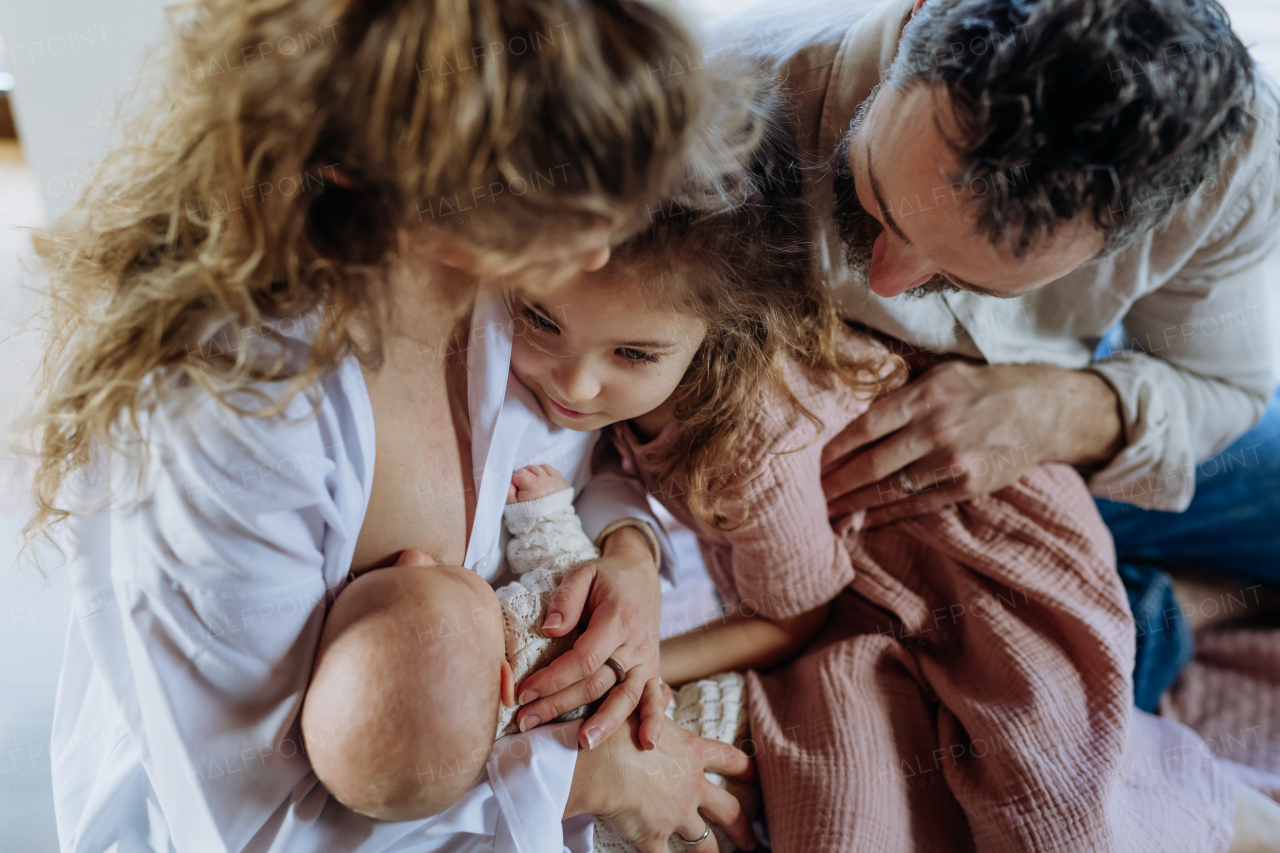 Mother breastfeeding newborn, big sister looking at new baby in mom's arms. Strong family, bonding, parents' unconditional love for their children.