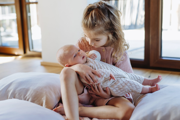 Portrait of big sister holding newborn sister. Girl carefully cuddling little baby. Sisterly love, joy for new family member.