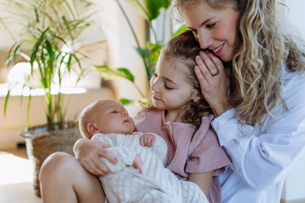 Girl hodling little baby, mother looking. Big sister meeting newborn baby syster, enjoying together time. Family bonding.