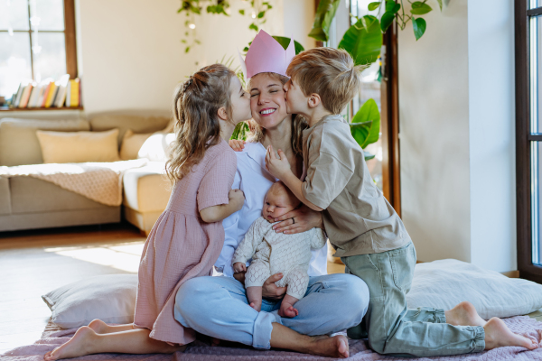 Mother after giving birth as a queen. Daughter and son kissing mom with paper crown on head. Admiration and love for mothers, concept of Mother's Day and women's strength.